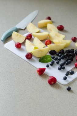 Dilimlenmiş taze elma, çilek, yaban mersini ve böğürtlen, nane yaprakları çevresinde, taze yaz meyve, yan bıçak