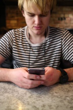 Telefonunu masada bakarak bir genç adam.