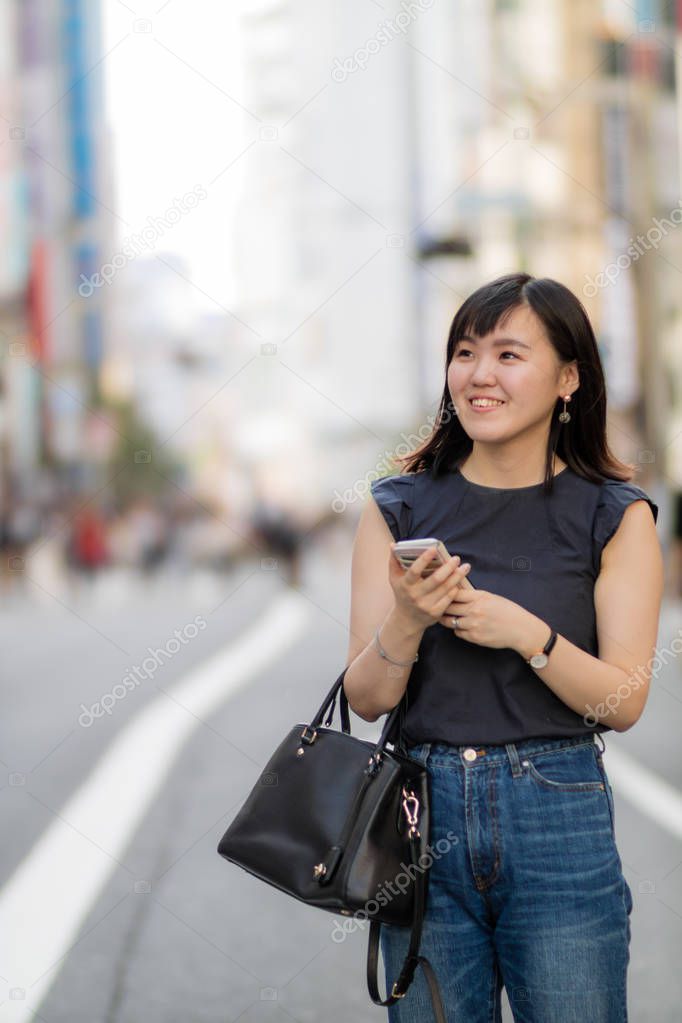 A beautiful Japanese Lady in the City holding her mobile phone.