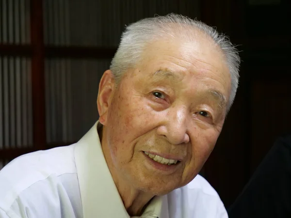 Et portrett av en eldre asiatisk mann som smiler til kameraet.. stockbilde