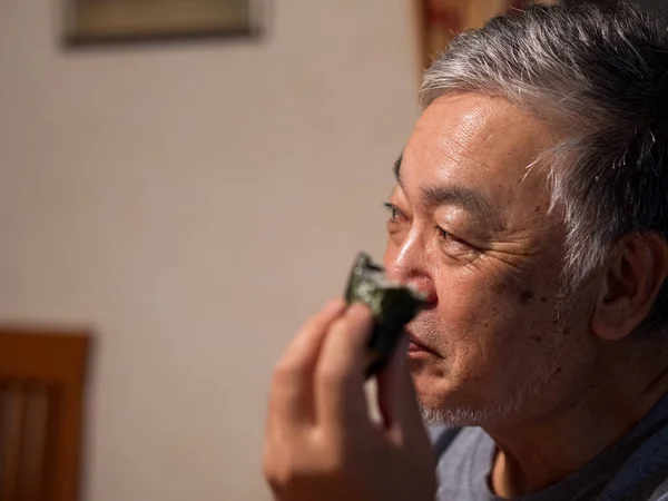 An older man enjoying an onigiri rice ball in his home