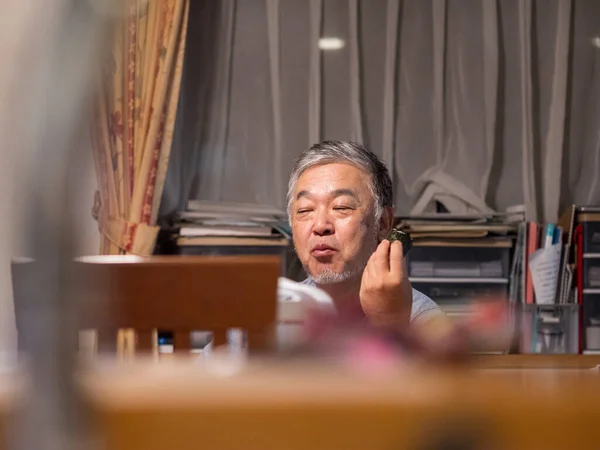 An older man enjoying an onigiri rice ball in his home