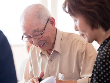 Yaşlı bir adam büyük bir ilgiyle aldığı bir şeye bakıyor.