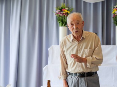 Yaşlı bir Asyalı aile etkinliğinde konuşma yapıyor.