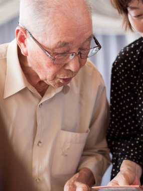 Yaşlı bir adam büyük bir ilgiyle aldığı bir şeye bakıyor.