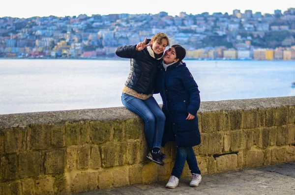 日没時の街を背景に笑顔の2人の若い女性 背景の青い海 — ストック写真