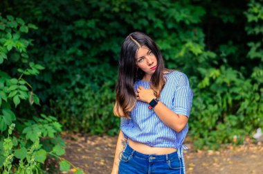 Kıvırcık siyah saçlı, dövmeli genç kızın portresi, kameraya dikkatlice bakıyor.