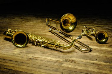 Yellow brass and wind instruments - saxophone, trombone, trumpet on a wooden stage with backlight clipart