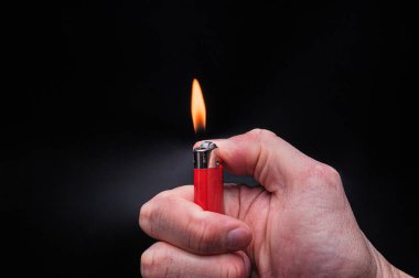 Avrupalı beyaz adamın eli, izole edilmiş siyah arka planda yanan kırmızı bir çakmak tutuyordu.