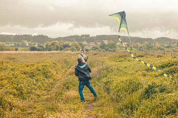 mother and her son fly a kite into the sky in the field in the rain