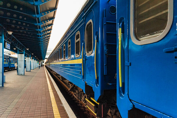Поезд пассажирских вагонов синей железной дороги стоит рядом с платформой на железнодорожной станции. Киев, Украина