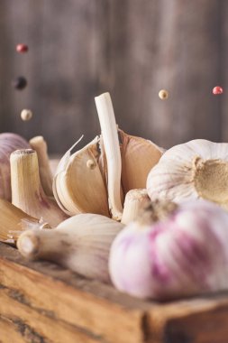 Yakın çekim görünümünü bir sürü taze Çiğ sarımsak ampuller ahşap kutu ve düşen siyah biber rustik gri arka plan üzerinde