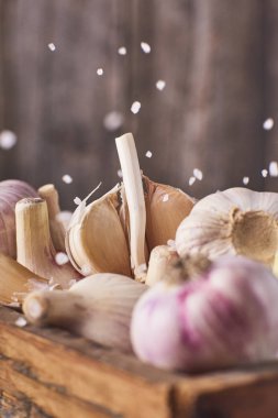Bir sürü ahşap kutu ve düşen deniz tuzu taze Çiğ sarımsak ampuller rustik gri arka plan üzerinde görmek