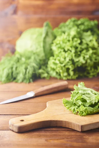 Ahşap arka plan üzerinde bıçak ile kesme tahtası üzerinde marul yaprakları. Karışık hazırlanması. Salata türleri arka plan üzerinde bırakır. Marul, roka, friz, kırmızı sert marul, lahana, ıspanak.