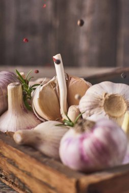 Yakın çekim görünümünü bir sürü taze Çiğ sarımsak ampuller ahşap kutu ve düşen siyah biber rustik gri arka plan üzerinde