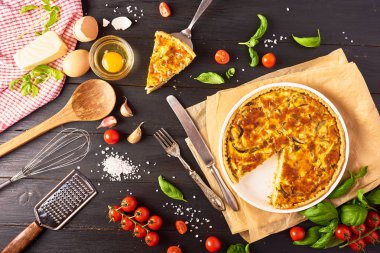 Bir parça ev yapımı quiche lorraine tavuk, mantar ve peynir, mutfak eşyaları ve siyah ahşap arka plan yemek pişirmek için malzemeler. Fransız mutfağı
