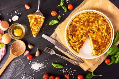 Bir parça ev yapımı quiche lorraine tavuk, mantar ve peynir, mutfak eşyaları ve siyah ahşap arka plan yemek pişirmek için malzemeler. Fransız mutfağı