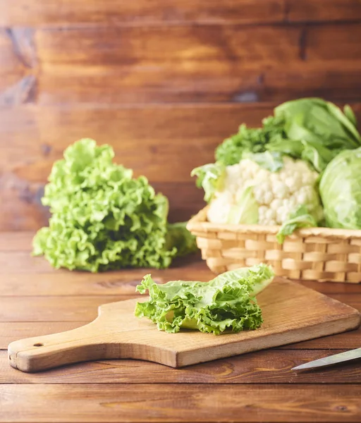 Lettuce leaves on cutting board with knife on wooden background. Preparation of salade. Various types of salad leaves on background. Lettuce, arugula, frieze, red hard lettuce, cabbage, spinach.