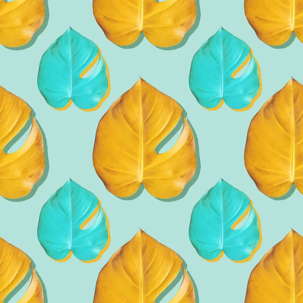 Tropical yellow and turquoise monstera leafes on turquoise background. Seamless color pattern