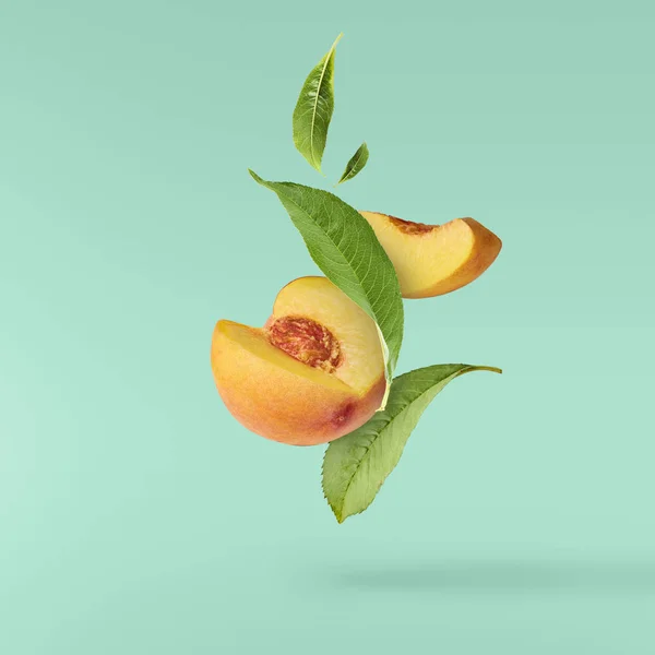 Flying fresh ripe peach with green leaves isolated on turquoise background. Concept of food levitation, high resolution image
