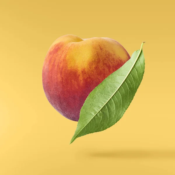 Flying fresh ripe peach with green leaves isolated on yellow background. Concept of food levitation, high resolution image