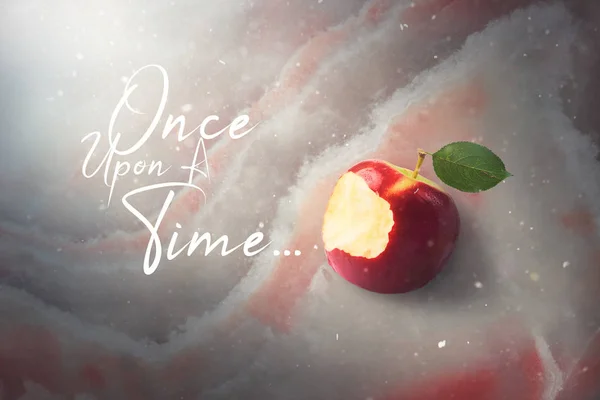 Fairy tale tale concept with poisoned bitten red apple laying on marble, sunlight and defocused falling snow, top view, high quality image. Once upon a time.