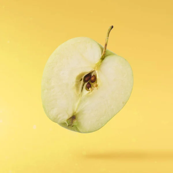 Green fresh cut apple Flying in air over yellow background, food levitation concept, high quality