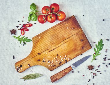 Boş kesme tahtası ve taze domates, baharatlar, fesleğen, roka ve bıçak rustik arka planda, üstten görünüm