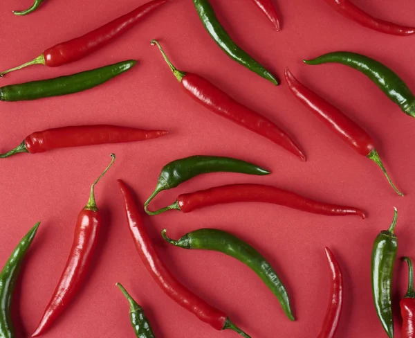 red hot chili peppers, spices concept, decorative pattern of red hot chili with green tails on red , top view, flat lay
