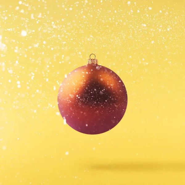 Christmas concept.  Creative Christmas conception made by falling in air shiny bauble over yellow background. Minimal concept