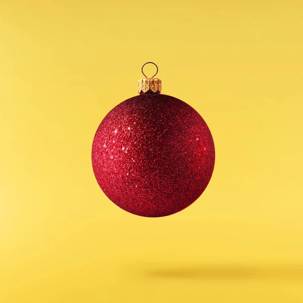 Christmas concept.  Creative Christmas conception made by falling in air shiny bauble over yellow background. Minimal concept