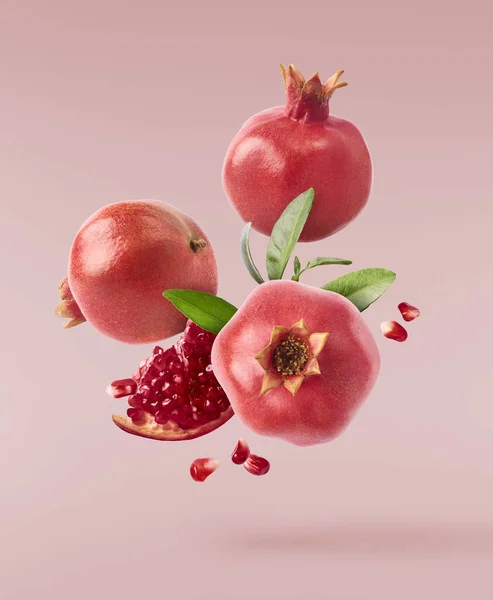 Flying in air fresh ripe whole and cut pomegranate with seeds and leaves isolated on pastel pink background. High resolution image