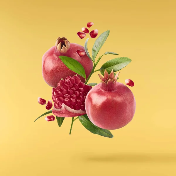 Flying in air fresh ripe whole and cut pomegranate with seeds and leaves isolated on yellow background. High resolution image