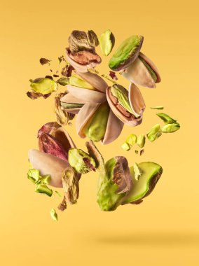 Havada taze çiğ olarak uçuyor ve sarı arka planda izole edilmiş fındık fıstıkları kırıyor. Pistachios kavramı yakın plan parçalara ayrıldı. Yüksek çözünürlük