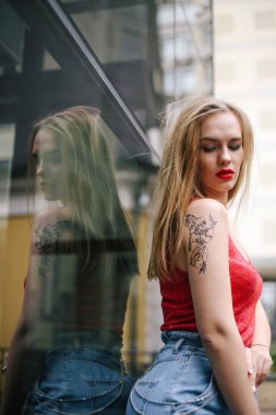 Cam bir binanın arka planında kırmızı tişört ve kot pantolon giymiş güzel bir kız model. Sokak tarzı, moda, yaşam tarzı