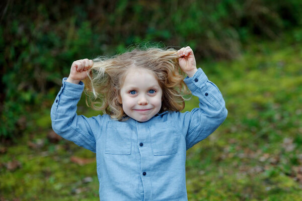 счастливый маленький мальчик показывает длинные светлые волосы на открытом воздухе
 