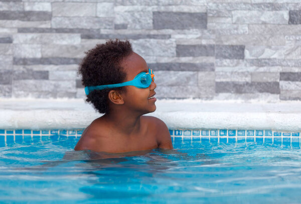 cute happy Afro-American kid with orange sleeve floats swimming in the pool 