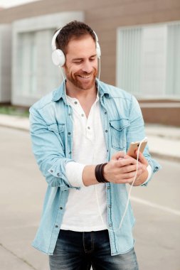 kulaklıklar ve sokakta smartphone üzerinden müzik dinlemek denim giyim eşyası yakışıklı genç