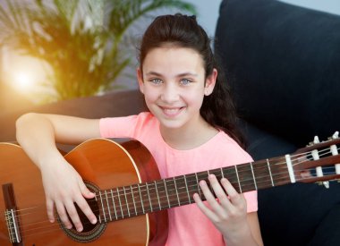 Evdeki kanepede gitar çalan genç bir kız.