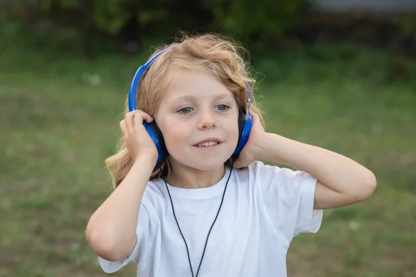 青い音楽を聴いている長い髪の面白い子供は 公園で携帯電話を持っていました — ストック写真