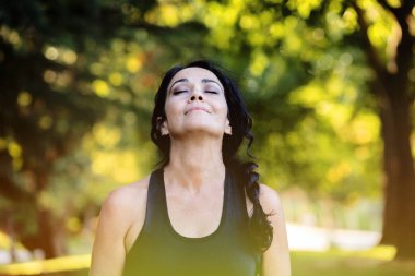 Esmer kadın parkta yoga yapıyor.