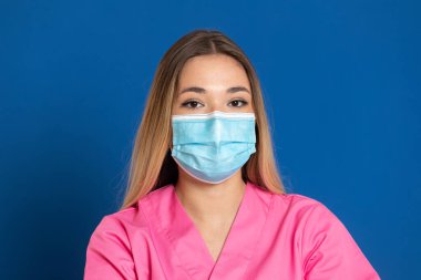 Maske takan genç bir doktor ve mavi arka planda pembe üniformalı.