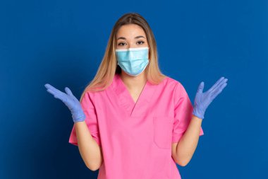 Maske takan genç bir doktor ve mavi arka planda pembe üniformalı.
