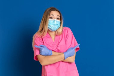 Maske takan genç bir doktor ve mavi arka planda pembe üniformalı.