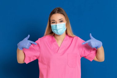 Maske takan genç bir doktor ve mavi arka planda pembe üniformalı.