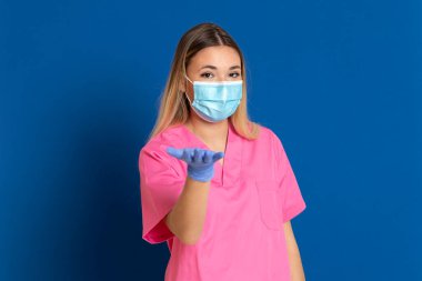 Maske takan genç bir doktor ve mavi arka planda pembe üniformalı.