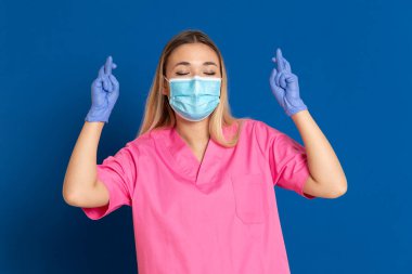 Maske takan genç bir doktor ve mavi arka planda pembe üniformalı.