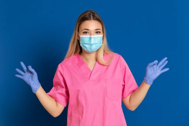 Maske takan genç bir doktor ve mavi arka planda pembe üniformalı.