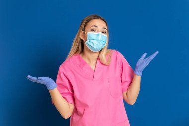 Maske takan genç bir doktor ve mavi arka planda pembe üniformalı.