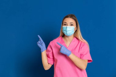 Maske takan genç bir doktor ve mavi arka planda pembe üniformalı.